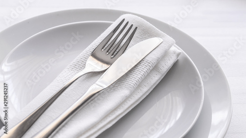 Close up of silverware fork and knife with napkin on white porcelaine plate. Copy space. Restaurant dinning concept.