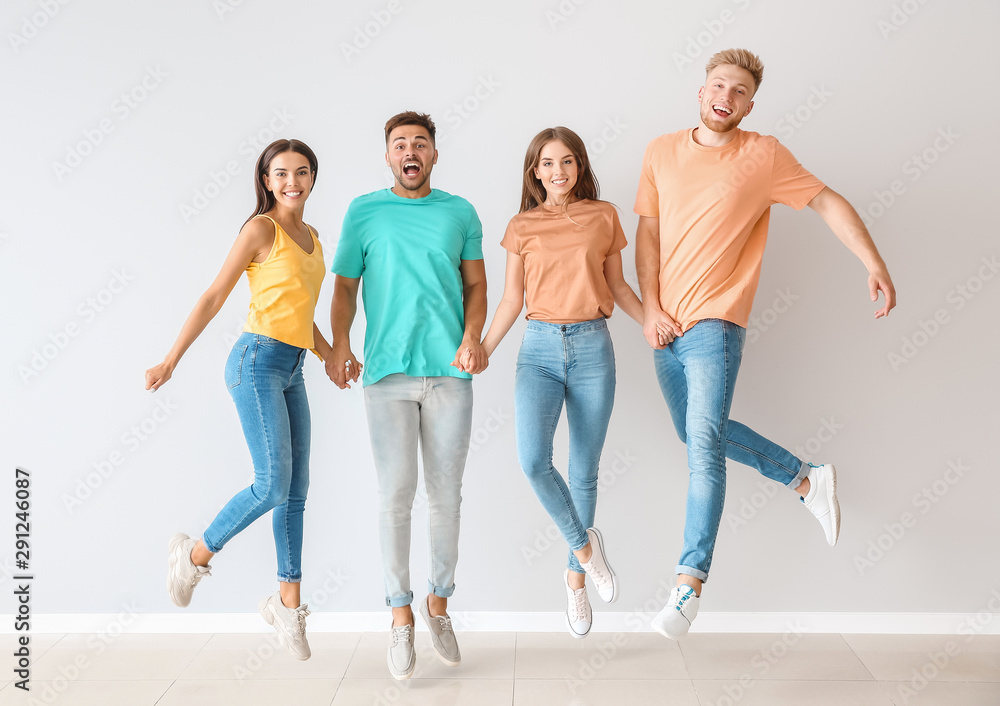 Fototapeta premium Group of jumping young people in stylish casual clothes near light wall