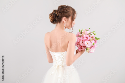 Canvas Print Beautiful young bride with wedding bouquet on light background, back view