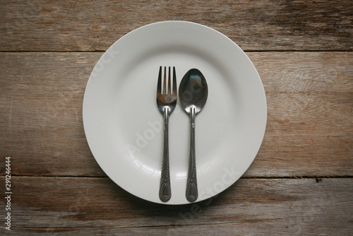 A white plate with spoon and fork on wooden background.