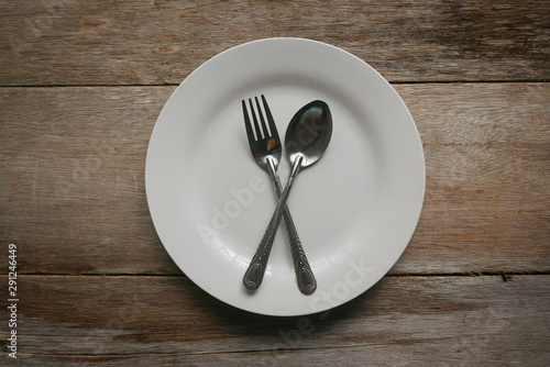 A white plate with spoon and fork on wooden background.