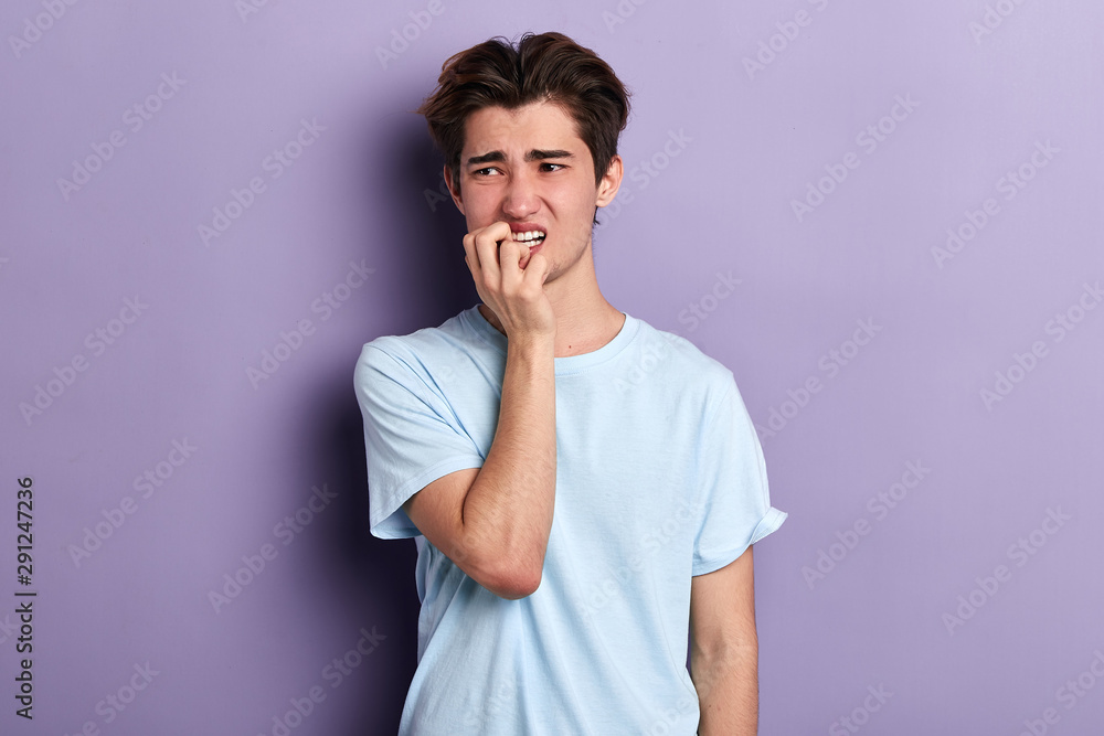 puzzled nervous man biting his nails , expressing negative feeling and emotion isolated on blue background with copy space, close up portrait puzzled nervous man biting his nails , expressing negative feeling and emotion isolated on blue background with copy space, close up portrait