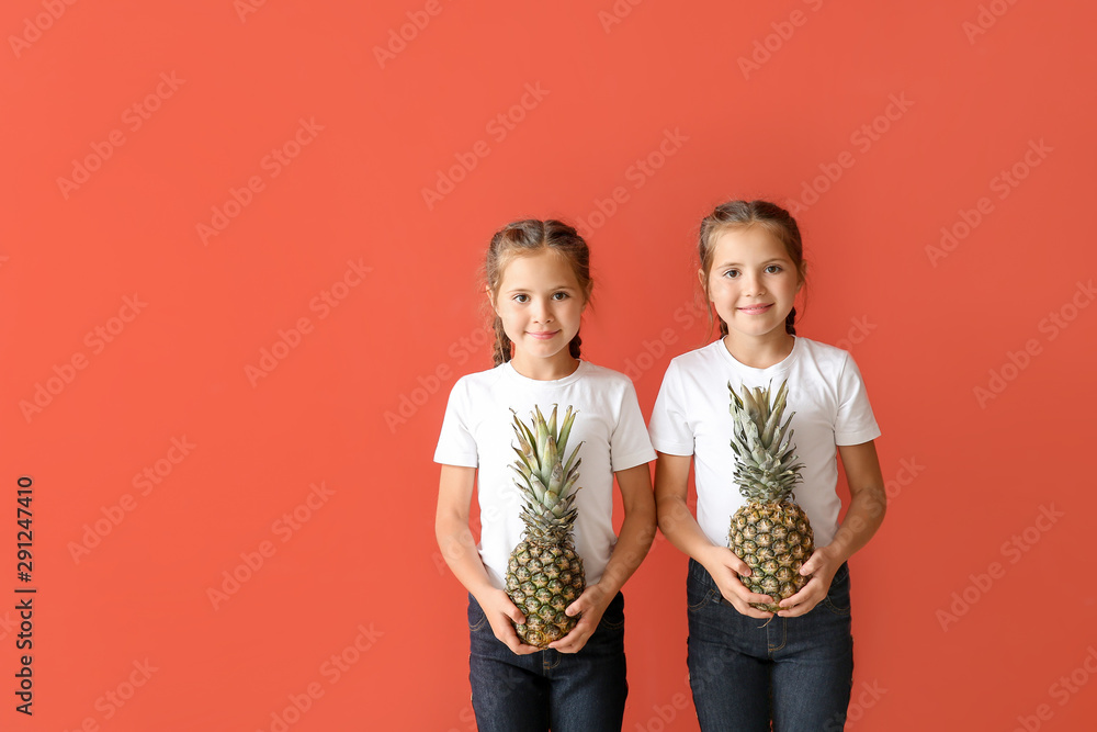 Portrait of cute twin girls with pineapples on color background - obrazy, fototapety, plakaty 