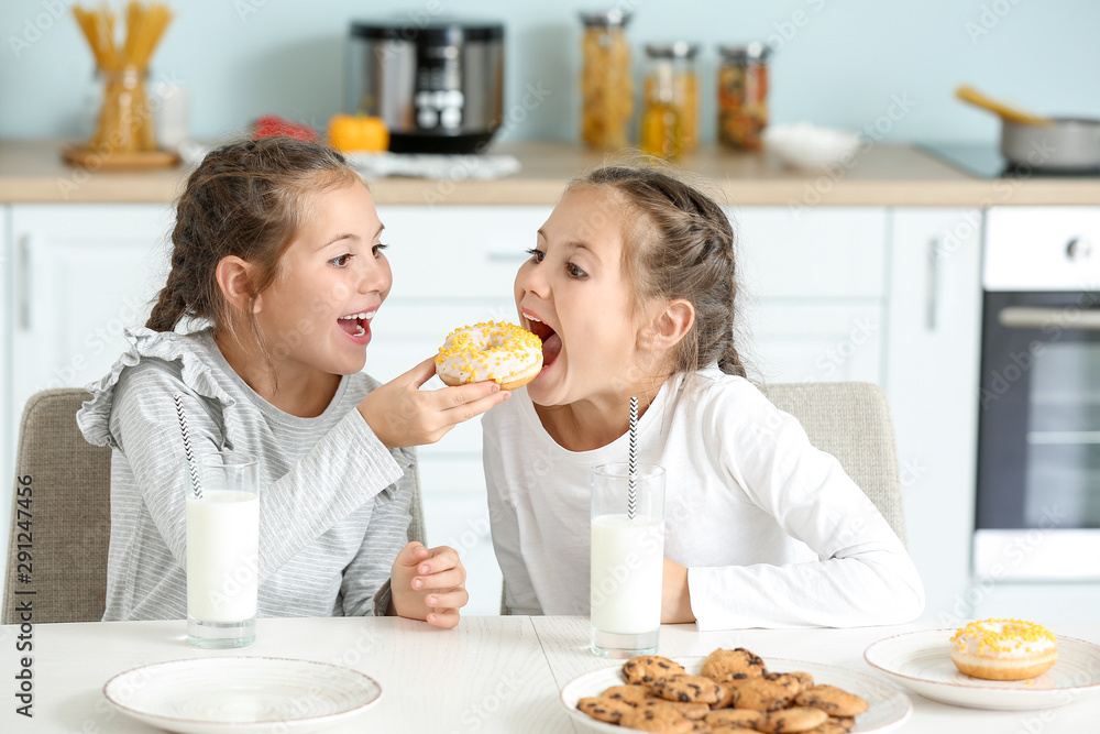 Portrait of cute twin girls eating donuts with milk in kitchen Portrait of cute twin girls eating donuts with milk in kitchen