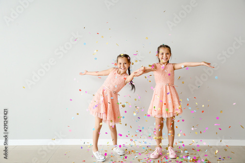 Portrait of happy twin girls with falling confetti near light wall