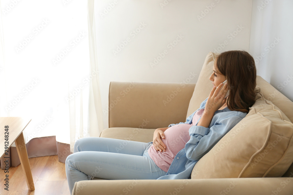 Beautiful pregnant woman talking by phone while sitting on sofa at home Beautiful pregnant woman talking by phone while sitting on sofa at home
