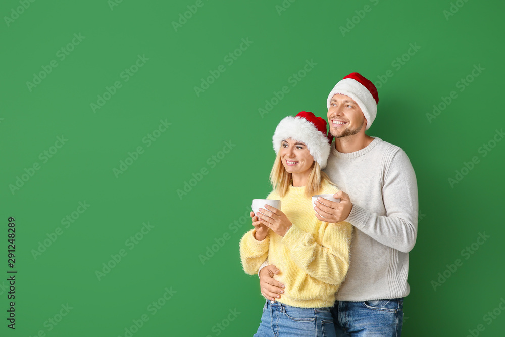 Happy couple in Santa hats drinking hot chocolate on color background Happy couple in Santa hats drinking hot chocolate on color background