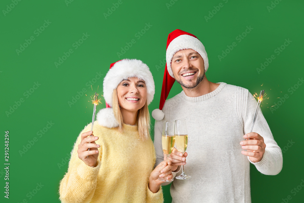 Happy couple in Santa hats, with champagne and sparklers on color background Happy couple in Santa hats, with champagne and sparklers on color background