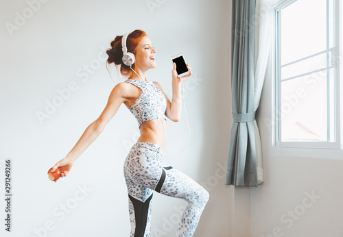 Full length body of beautiful woman wear earsphones lisening music and dancing in her room at home with apple in her hand. Happiness woman concept photo