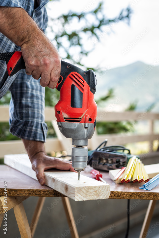 Adult craftsman carpenter with electric drill works makes a hole on a wooden table. Housework do it yourself. Stock photography.