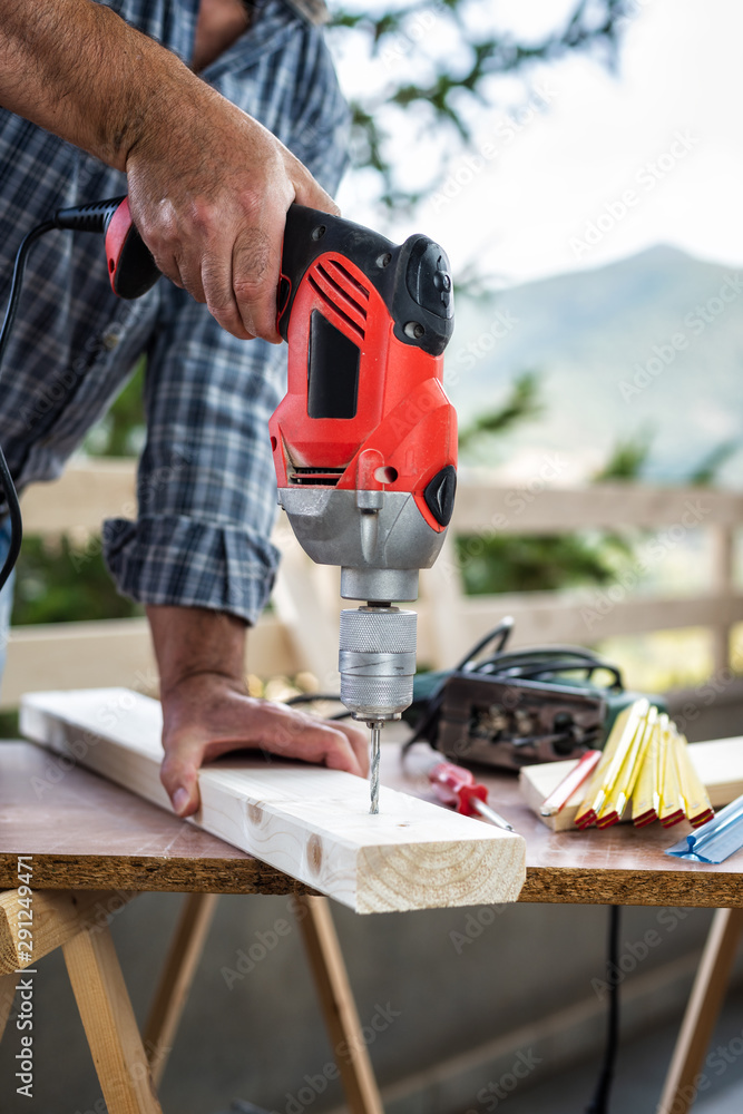 Adult craftsman carpenter with electric drill works makes a hole on a wooden table. Housework do it yourself. Stock photography.