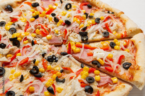 italian sliced pizza with corn, sweet pepper and olives, on a wooden board, macro