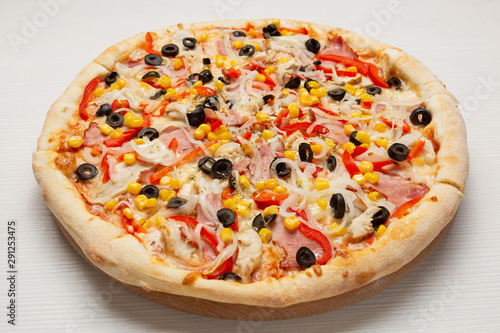 Italian pizza with slices of sausage, tomatoes, sweet pepper and corn, on a wooden board