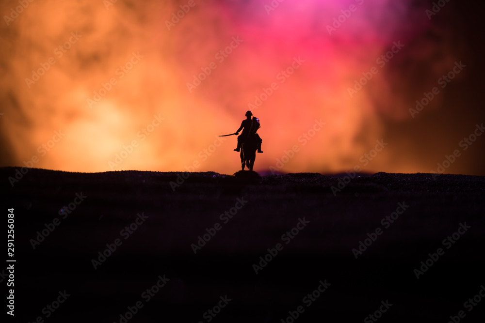 World war officer (or warrior) rider on horse with a sword ready to fight and soldiers on a dark foggy toned background. Battle scene battlefield of fighting soldiers.