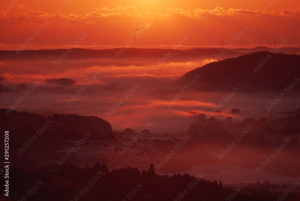 Obraz premium 雲海に沈む町。山間部の町（日本）に発生した雲海が、朝日で真っ赤に染まる風景写真