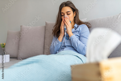 Woman with an inhaler. Portrait of a young woman doing inhalation at home. Use nebulizer and inhaler for the treatment. Young woman inhaling through inhaler mask lying on the couch