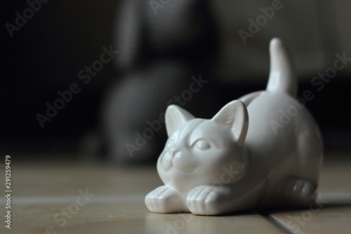 A white cat-shaped penny bank with a grey dog toy in the backround.