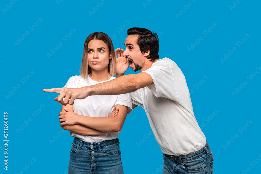 Bearded man with mustaches in white t-shirt tells secret to a young blond girl in white t-shirts and blue jeans and poinitng with a finger at some object. Concept of secret telling. Bearded man with mustaches in white t-shirt tells secret to a young blond girl in white t-shirts and blue jeans and poinitng with a finger at some object. Concept of secret telling.