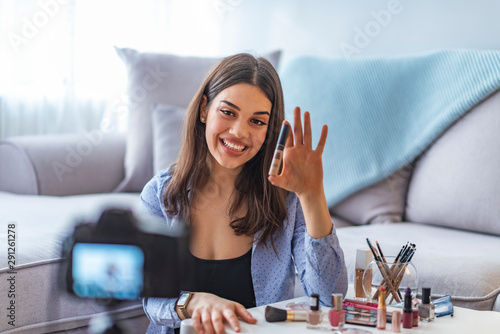 Happy smiling woman or beauty blogger with bronzer, brush and camera recording tutorial video at home. photo