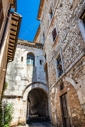 A characteristic glimpse of the city of Amelia, in Umbria. The cobbled alley, the stone and brick walls of the old houses in the historic center. A small gallery with arch.