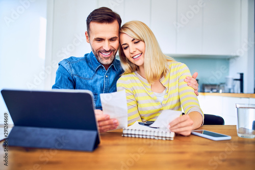 Happy couple managing home finances looking at receipts and tablet