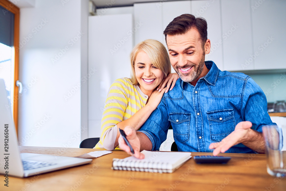 Fototapeta premium Happy couple looking at notebook in awe while managing home finances