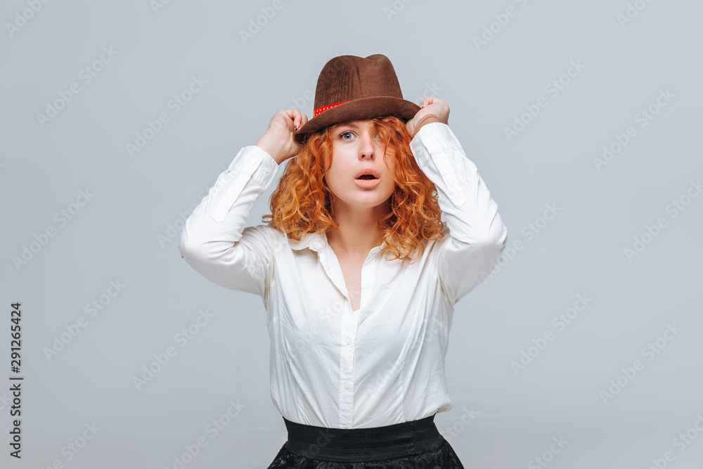 Red-haired joyful girl in a brown hat on a gray background in a white shirt Red-haired joyful girl in a brown hat on a gray background in a white shirt