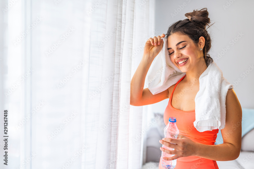 Jogger run runner energy sweaty yoga vitality wellness concept. Tired happy girl wiping sweat with towel in in eco modern interior home studio. Fit young woman drinking water at the home. Jogger run runner energy sweaty yoga vitality wellness concept. Tired happy girl wiping sweat with towel in in eco modern interior home studio. Fit young woman drinking water at the home.