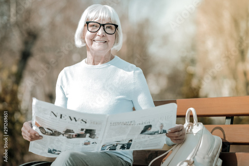 Foto Beaming elegant elderly missis holding paper in the park