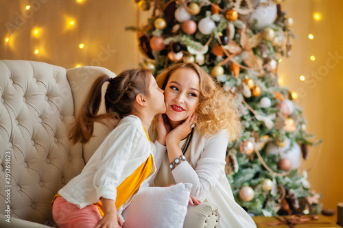 daughter kisses mom on the cheek near the Christmas tree