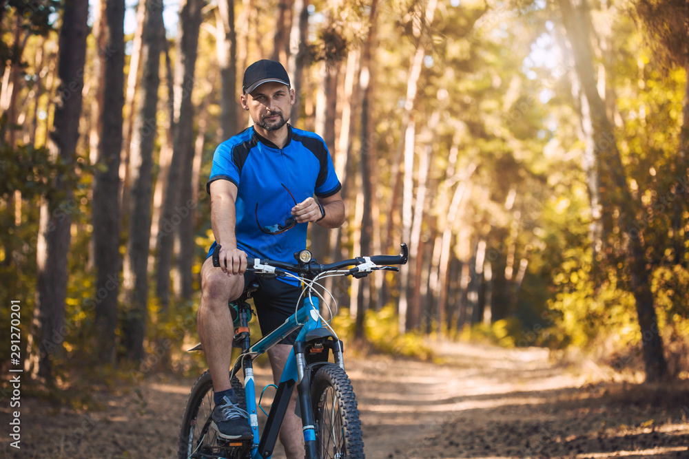 Happy bearded man cyclist rides in the sunny forest on a mountain bike. Adventure travel.