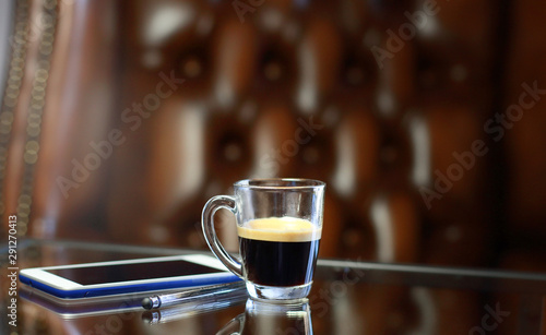 Cup of coffee with the phone on the glass table