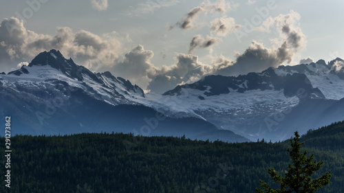 View of snow capped mountain peaks, across an alpine forest, set against an interesting sky.  The mountains are near Whistler, in British Columbia, Canada © parkerspics