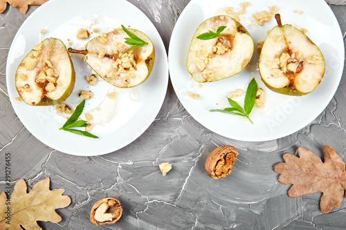 Tasty roast pears with honey and walnuts on white plates on grey background table. Top view. Flat lay. Copy space.