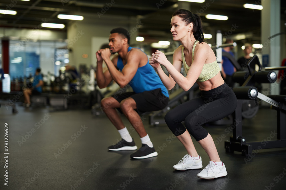 Side view portrait of sportive couple doing squats during fitness workout in modern gym, copy space