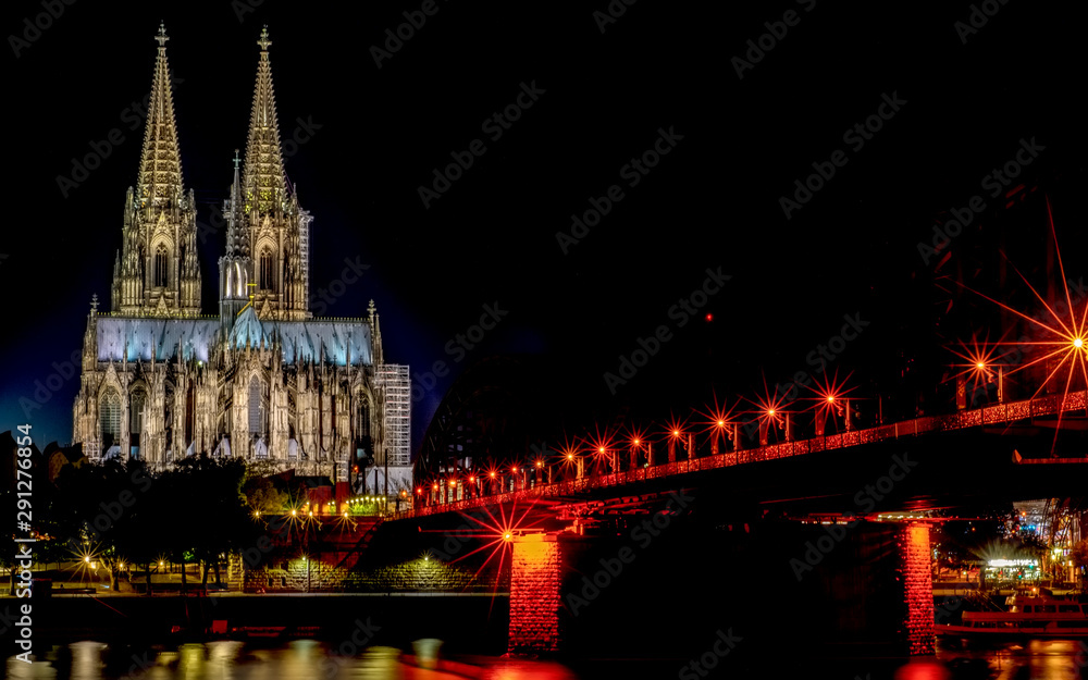 Obraz premium Night View of Cologne Cathedral (Kolner Dom) and Rhine river under the Hohenzollern Bridge, Cologne city skyline at night, North Rhine Westphalia region, Germany.