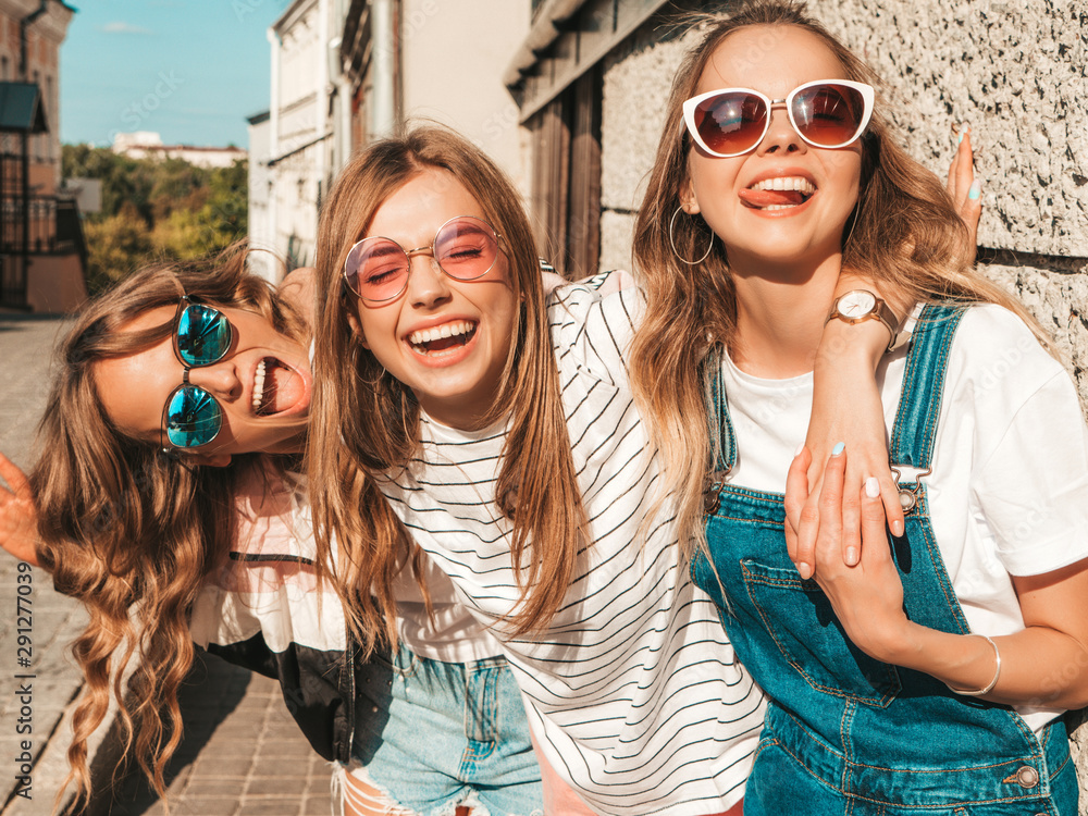 Portrait of three young beautiful smiling hipster girls in trendy summer clothes. Sexy carefree women posing near wall in the street.Positive models having fun in sunglasses - obrazy, fototapety, plakaty 