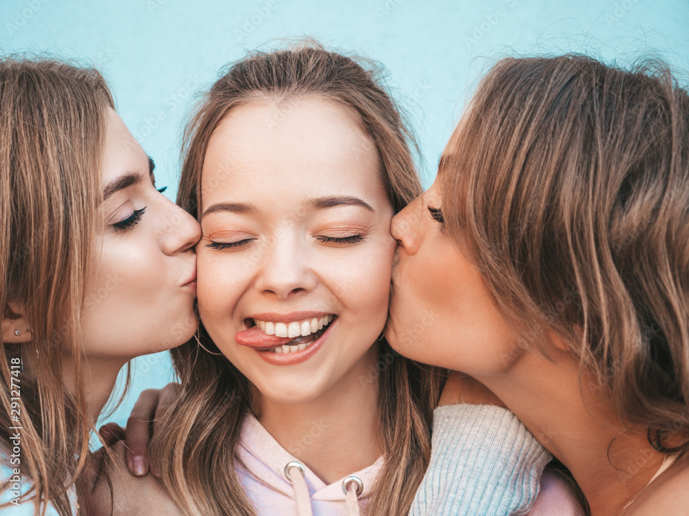 Portrait of three young beautiful smiling hipster girls in trendy summer clothes. Sexy carefree women posing in the street.Positive models kissing their friend in cheek Portrait of three young beautiful smiling hipster girls in trendy summer clothes. Sexy carefree women posing in the street.Positive models kissing their friend in cheek