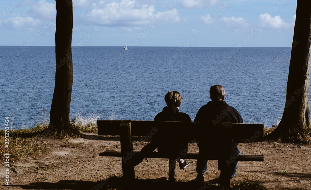 Zwei ältere Menschen sitzen auf einer Bank und schauen auf das Meer.