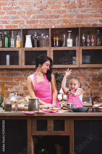 Young beautiful mother and her little daughter cooking together at the kitchen