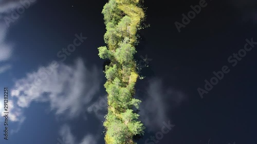 A small island with trees in the form of a strip surrounded by blue water and reflected sky. Aerial view.