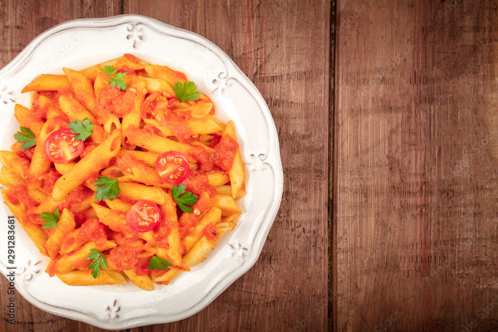 Penne pasta close-up. Pasta with tomato sauce and parsley, shot from the top on a dark rustic wooden background with a place for text Penne pasta close-up. Pasta with tomato sauce and parsley, shot from the top on a dark rustic wooden background with a place for text