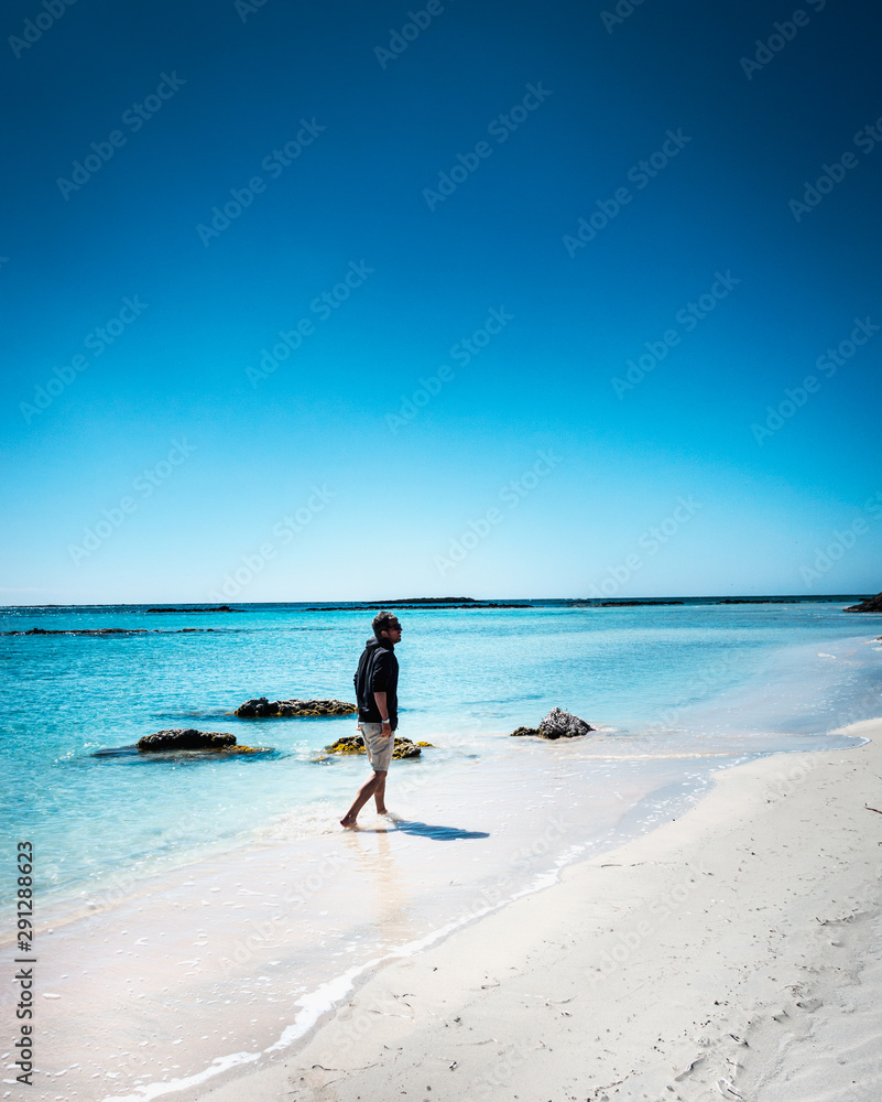 Young man walking on beach with hands in pocket Young man walking on beach with hands in pocket