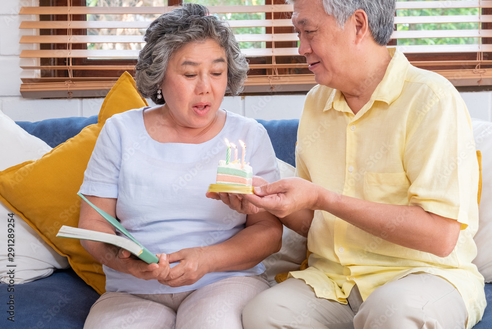 asian senior man surprise senior woman with birthday cake in living room at home.aging at home concept. asian senior man surprise senior woman with birthday cake in living room at home.aging at home concept.
