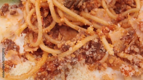 Extreme close-up reeling appetizing fresh spaghetti bolognese with parmesan surrounded by tomato sauce using fork. Eating tasty traditional Italian pasta food serving on plate