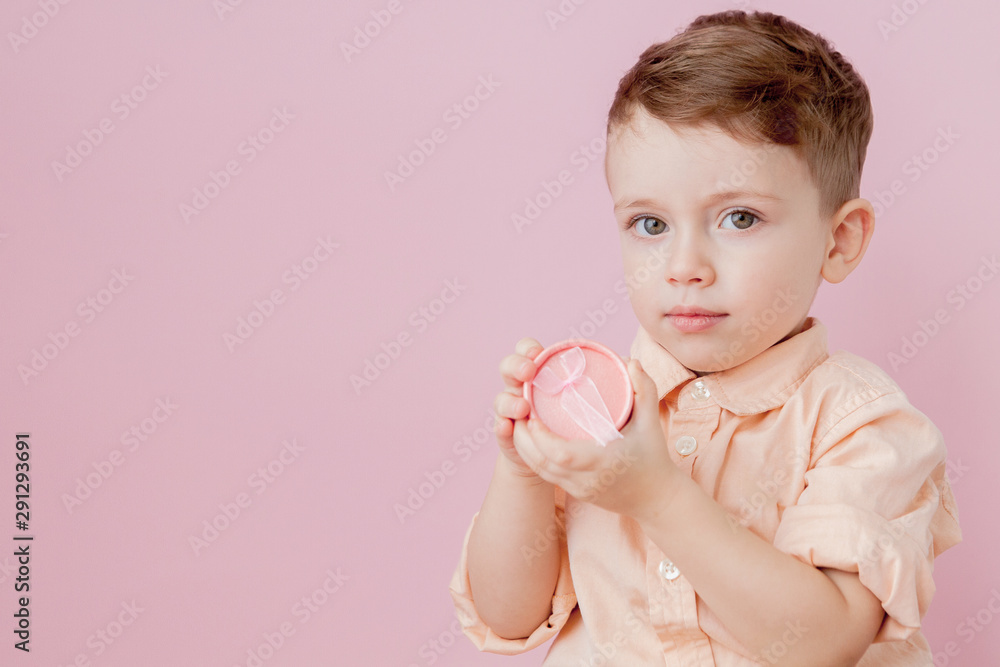 Happy little boy with a gift . Photo isolated on pink background. Smiling boy holds present box. Concept of holidays and birthday