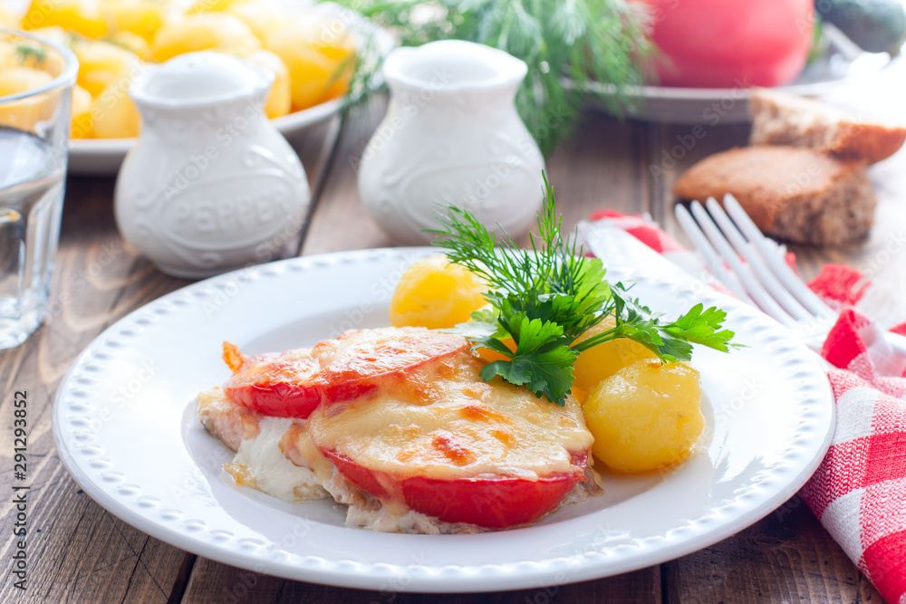 Baked pink salmon with tomato and cheese on a white plate with potatoes, horizontal Baked pink salmon with tomato and cheese on a white plate with potatoes, horizontal