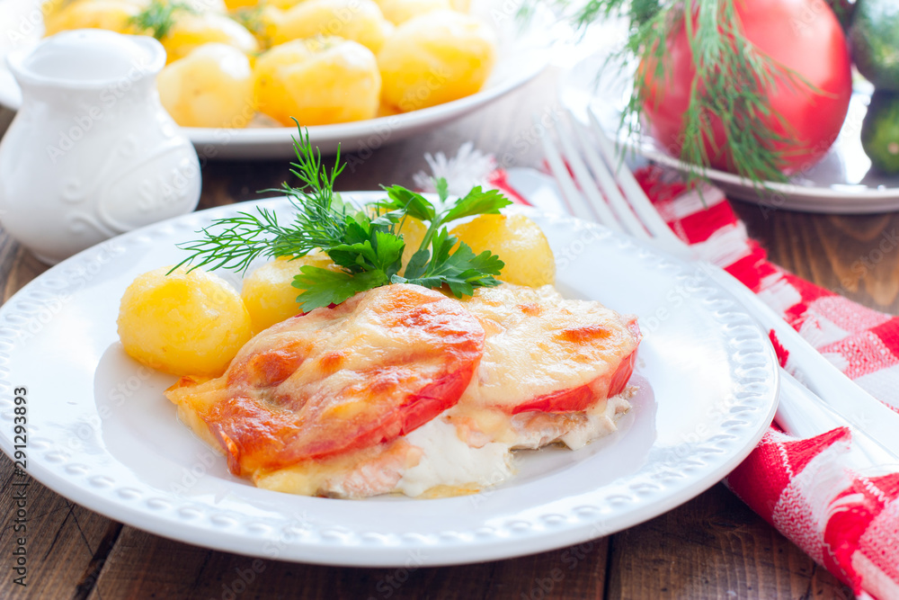 Baked pink salmon with tomato and cheese on a white plate with potatoes, horizontal Baked pink salmon with tomato and cheese on a white plate with potatoes, horizontal