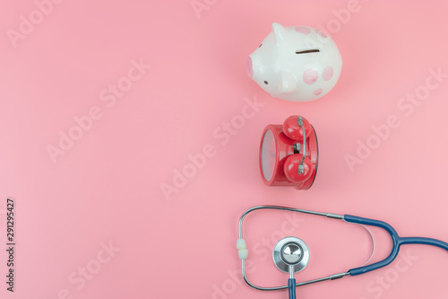 Top view with copy space of Piggi bank,red clock and stethoscope on the pink pastel background, Savings, Time and Health concept photo