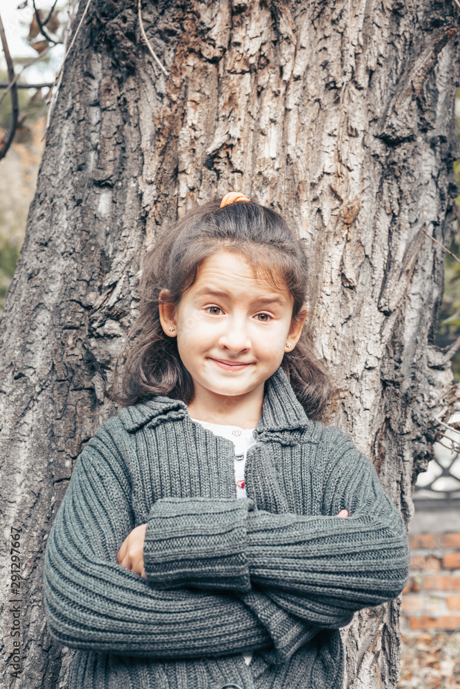 Cheerful cute girl. School age teenager girl stands near an old tree in autumn park Cheerful cute girl. School age teenager girl stands near an old tree in autumn park